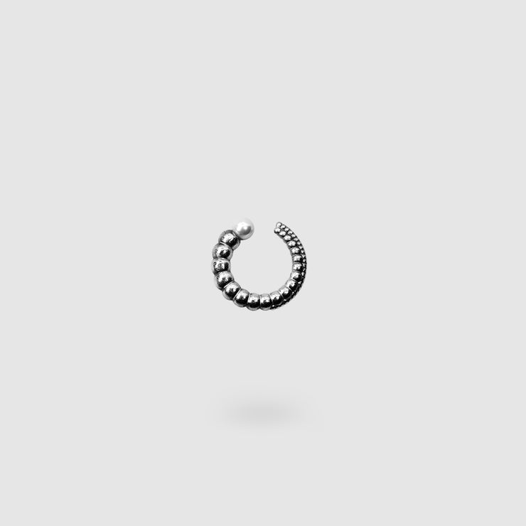 This sculptural ear cuff from the PHAOS collection reimagines the ancient granulation technique through digital design and contemporary craftsmanship. Designed to sit securely without a piercing, its fluid form curves around the ear and finishes with a luminous white glass pearl - adding a touch of shimmer to any look. Available in your choice of gold-plated brass or .925 silver.