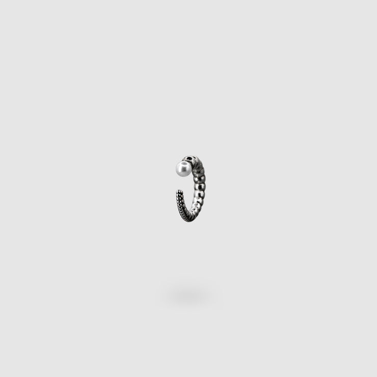 This sculptural ear cuff from the PHAOS collection reimagines the ancient granulation technique through digital design and contemporary craftsmanship. Designed to sit securely without a piercing, its fluid form curves around the ear and finishes with a luminous white glass pearl - adding a touch of shimmer to any look. Available in your choice of gold-plated brass or .925 silver.
