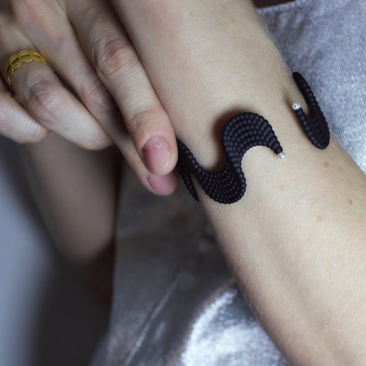 This lightweight cuff bracelet from the PHAOS collection is crafted from hand-dyed, 3D printed bioplastic and accented with glass pearls. Made from a renewable, plant-based polyamide derived from vegetable oil, each piece is hand-finished in your choice of colour; blending sustainable innovation with bold, contemporary design.