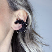 This sophisticated ear cuff from the PHAOS collection reimagines the ancient granulation technique through digital design and contemporary craftsmanship. Designed to sit securely without a piercing, its geometric shape curves around the ear. Hand-dyed and finished with care, each piece features a subtle touch of .925 silver.
