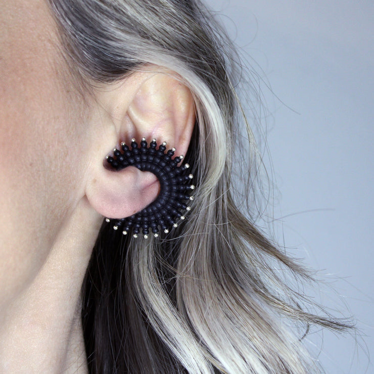 This sophisticated ear cuff from the PHAOS collection reimagines the ancient granulation technique through digital design and contemporary craftsmanship. Designed to sit securely without a piercing, its geometric shape curves around the ear. Hand-dyed and finished with care, each piece features a subtle touch of .925 silver.