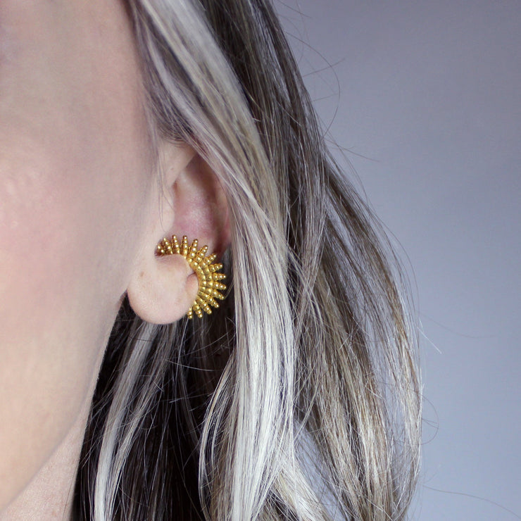 This sophisticated ear cuff from the PHAOS collection reimagines the ancient granulation technique through digital design and contemporary craftsmanship. Designed to sit securely without a piercing, its geometric shape curves around the ear. Available in your choice of gold-plated brass or .925 silver.