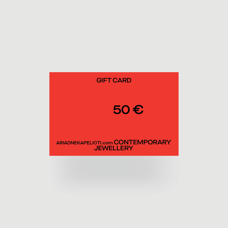 A thoughtful and versatile gift card from ARIADNE KAPELIOTI, valued at 50 EUR, adorned in red with "GIFT CARD" printed in black at the top and "50 €" prominently displayed in the center. The bottom of this stylish card features the black text "ARIADNEKAPELIOTI.com CONTEMPORARY JEWELLERY." Set against a light gray background, this no-strings-attached gift card is perfect for any occasion.